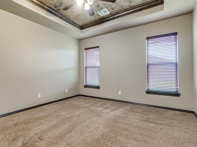 carpeted empty room with a ceiling fan, a tray ceiling, visible vents, and baseboards