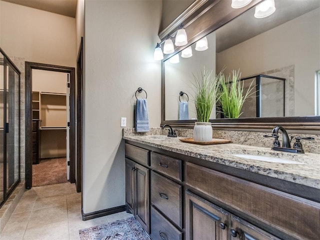 full bath with double vanity, a sink, a walk in closet, and a stall shower