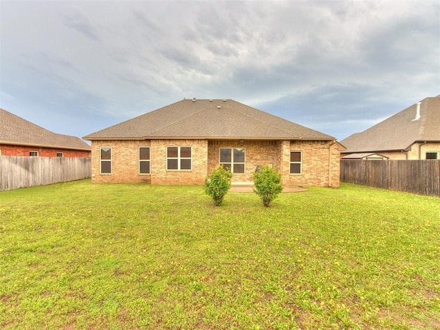 back of house featuring a fenced backyard, a yard, roof with shingles, and brick siding
