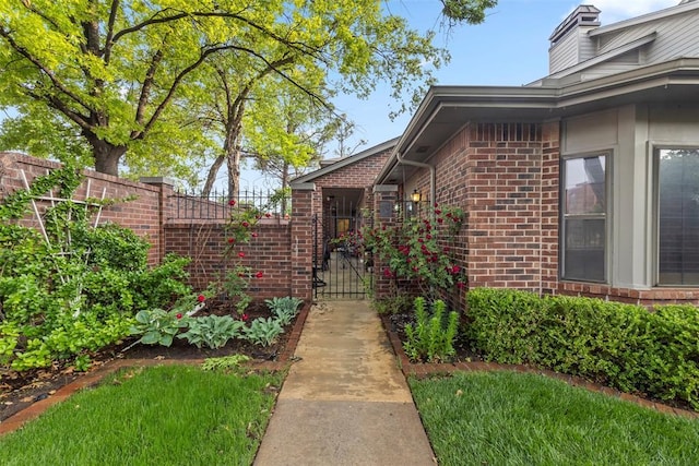 view of exterior entry with brick siding, fence, a chimney, and a gate