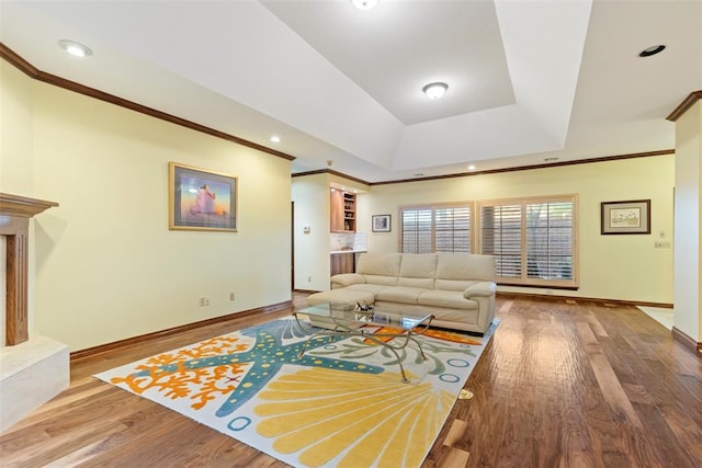 living area with crown molding, baseboards, wood finished floors, and a raised ceiling