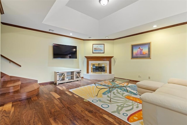 living room with crown molding, a raised ceiling, a premium fireplace, baseboards, and wood finished floors