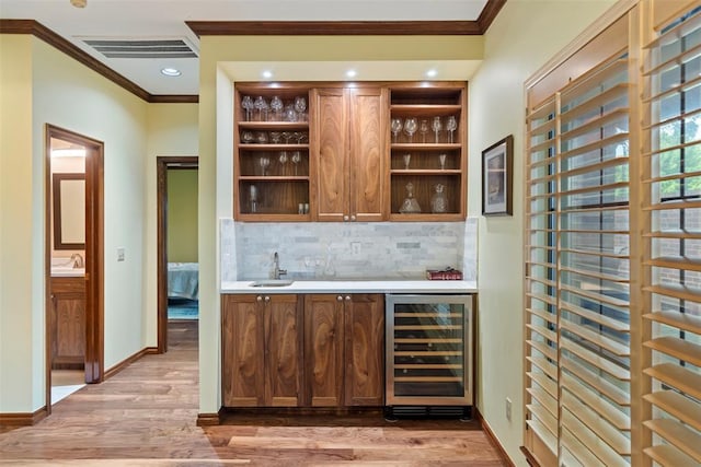 bar featuring crown molding, wet bar, light wood-style floors, and beverage cooler
