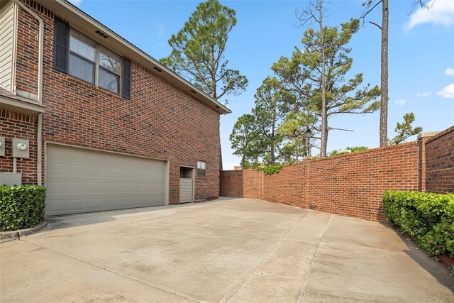 view of side of property featuring brick siding, an attached garage, fence, and concrete driveway