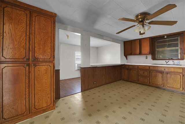 kitchen with brown cabinetry, a ceiling fan, light floors, light countertops, and a sink