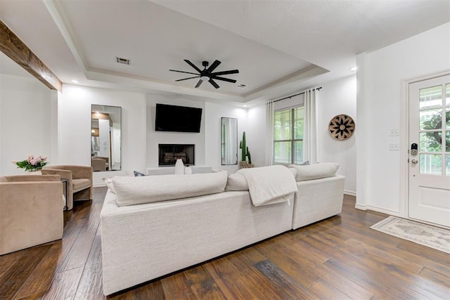 living room with visible vents, a ceiling fan, a tray ceiling, and dark wood-style floors