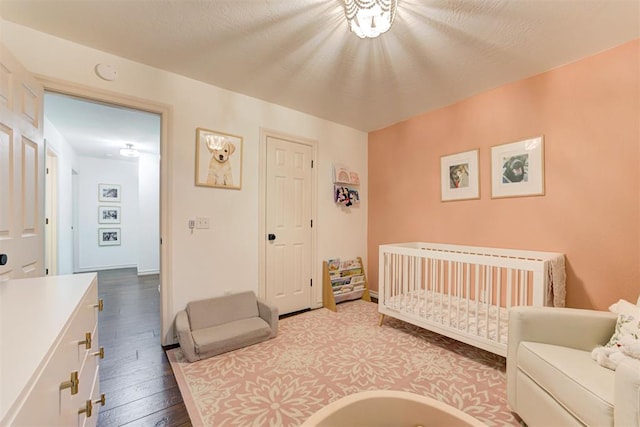 bedroom featuring a crib and dark wood-style flooring