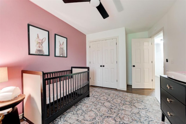 bedroom with ceiling fan, a crib, wood finished floors, and a closet