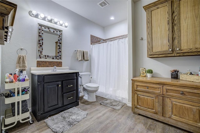 full bath with a shower with curtain, visible vents, wood finished floors, vanity, and toilet