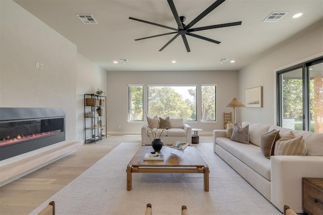 living room featuring a ceiling fan, visible vents, a healthy amount of sunlight, and light wood-type flooring