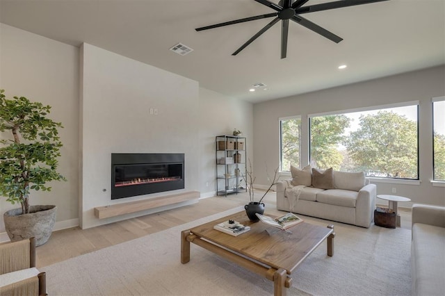 living area with visible vents, a glass covered fireplace, wood finished floors, baseboards, and a ceiling fan