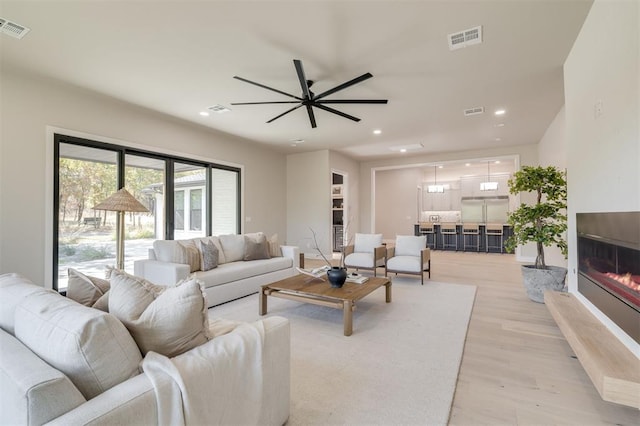 living area featuring visible vents, a ceiling fan, light wood finished floors, and a glass covered fireplace
