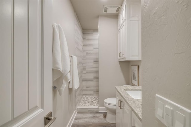bathroom featuring visible vents, vanity, wood finished floors, toilet, and tiled shower