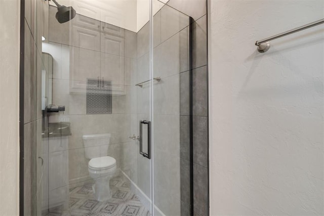 full bath with tile patterned floors, a stall shower, toilet, and tile walls