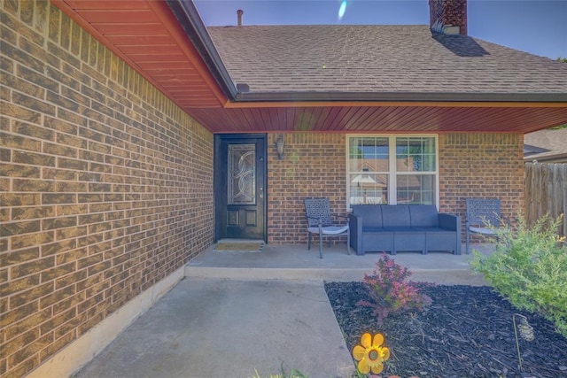 doorway to property featuring brick siding, an outdoor living space, roof with shingles, and a chimney