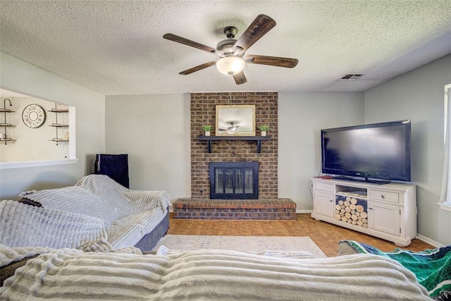 living room featuring ceiling fan, a textured ceiling, visible vents, a fireplace, and light wood-style flooring