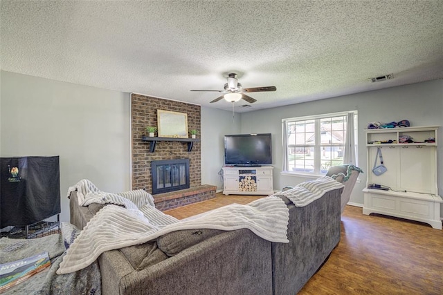 living room featuring visible vents, a brick fireplace, wood finished floors, ceiling fan, and a textured ceiling