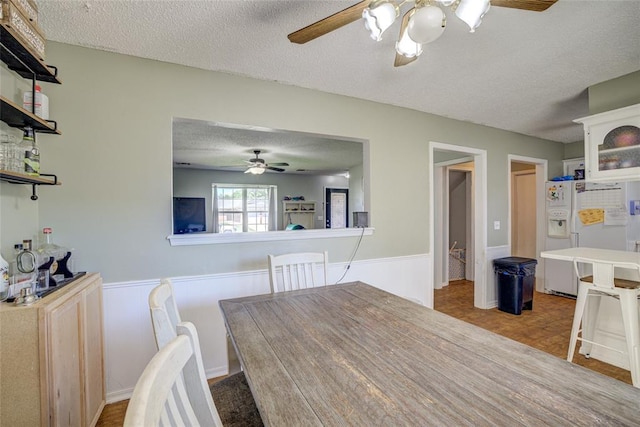 dining area with a ceiling fan, a textured ceiling, and a wainscoted wall