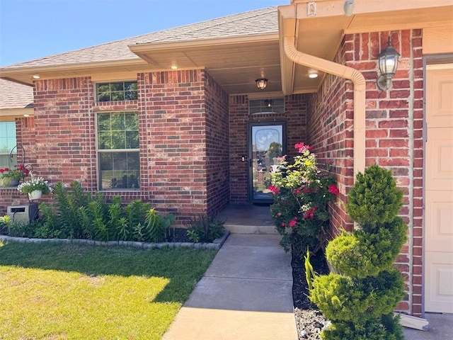 doorway to property with a lawn, brick siding, and a shingled roof