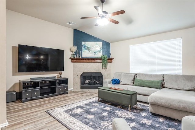 living area featuring ceiling fan, visible vents, a tiled fireplace, vaulted ceiling, and wood finished floors