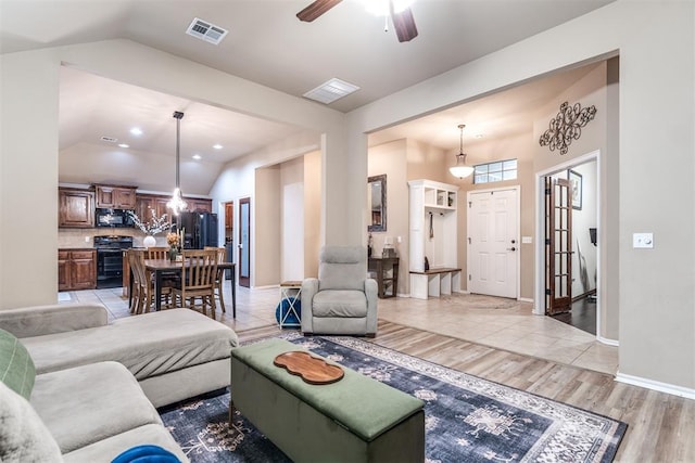 living area featuring visible vents, light wood-style flooring, lofted ceiling, and ceiling fan with notable chandelier