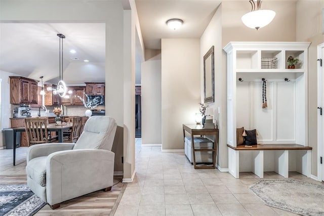 mudroom featuring light tile patterned floors, baseboards, vaulted ceiling, and a notable chandelier
