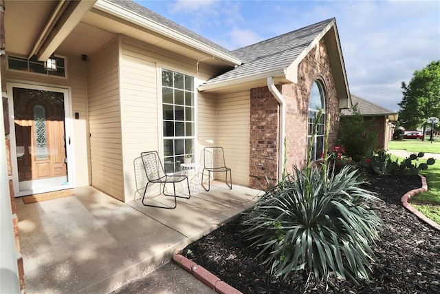 entrance to property with brick siding and a shingled roof