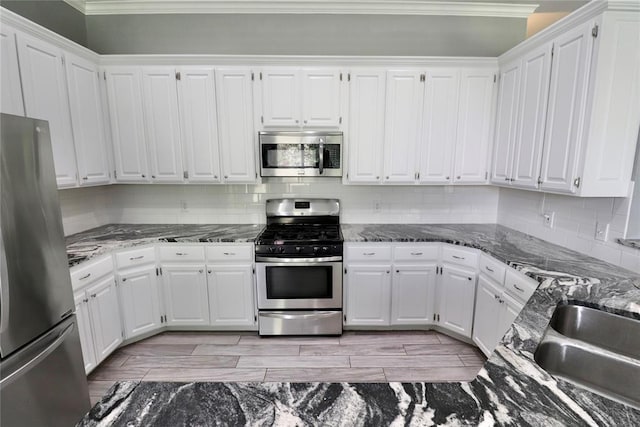 kitchen with crown molding, dark stone counters, white cabinetry, tasteful backsplash, and appliances with stainless steel finishes