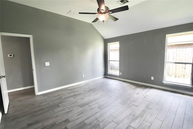 empty room with a ceiling fan, visible vents, vaulted ceiling, wood finished floors, and baseboards