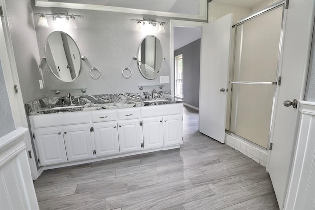 bathroom with a sink, a stall shower, double vanity, and wood finished floors