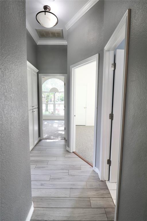 hallway with crown molding, a textured wall, baseboards, wood tiled floor, and visible vents