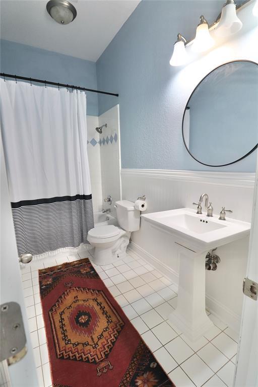 bathroom with toilet, tile patterned floors, wainscoting, and shower / tub combo