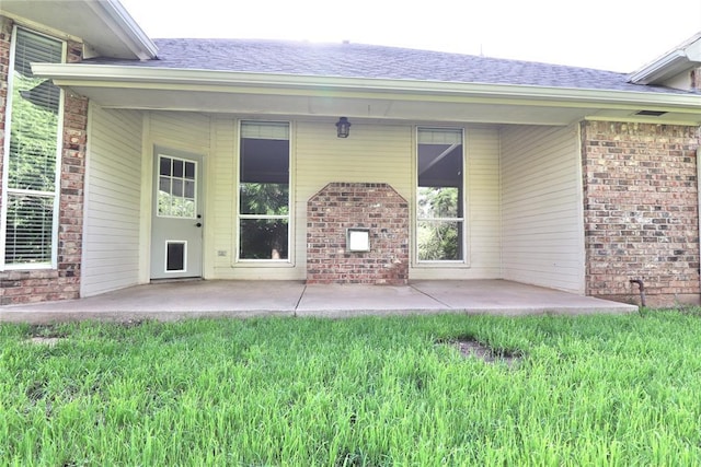 back of property with brick siding, a shingled roof, and a patio