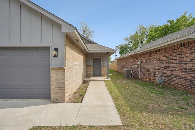 property entrance featuring board and batten siding, central AC unit, a garage, brick siding, and a yard