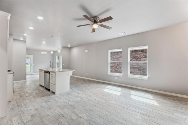 kitchen featuring a sink, light wood-style flooring, a ceiling fan, baseboards, and stainless steel dishwasher