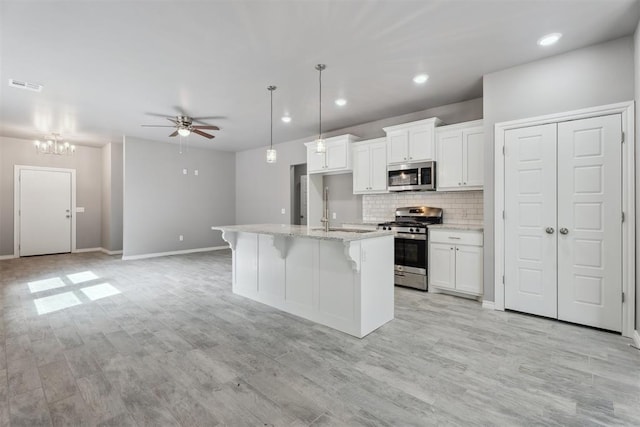 kitchen with white cabinets, stainless steel appliances, visible vents, and ceiling fan with notable chandelier