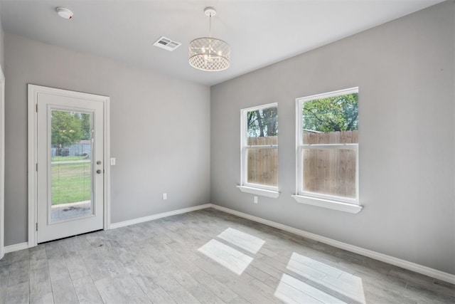 empty room with baseboards, visible vents, light wood finished floors, and a chandelier