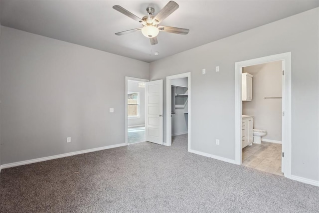 unfurnished bedroom with connected bathroom, baseboards, a spacious closet, and carpet