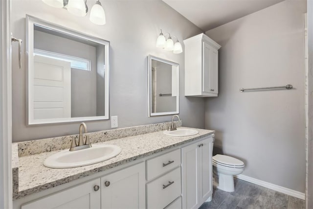 full bath with double vanity, toilet, a sink, and wood finished floors