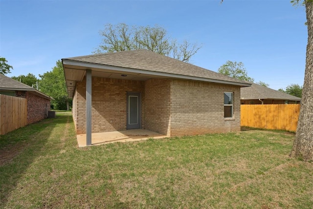 rear view of house with fence, a patio, brick siding, a shingled roof, and a lawn