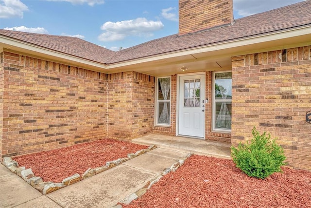 entrance to property with roof with shingles, a chimney, and brick siding