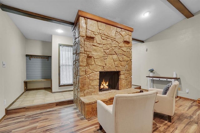 living area with a stone fireplace, lofted ceiling with beams, baseboards, and wood finished floors