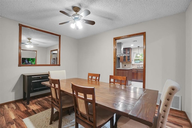 dining space with visible vents, light wood-style floors, baseboards, a textured ceiling, and a ceiling fan