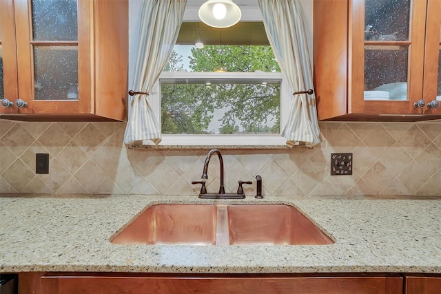 details featuring brown cabinetry, a sink, light stone countertops, and glass insert cabinets