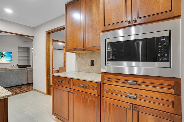 kitchen featuring light stone counters, tasteful backsplash, stainless steel microwave, and brown cabinets