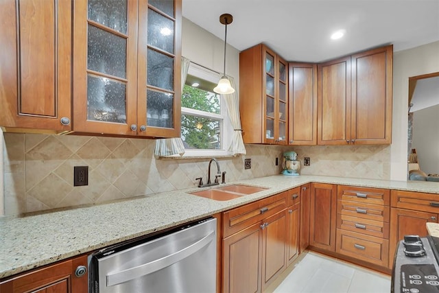kitchen featuring stainless steel dishwasher, a sink, brown cabinetry, and light stone countertops