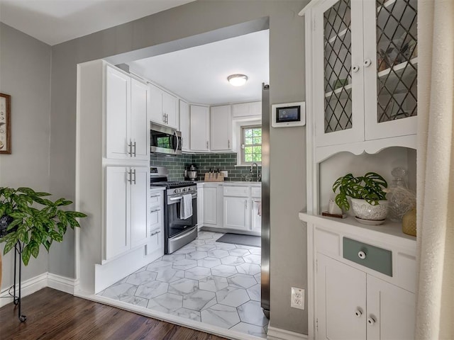 kitchen featuring tasteful backsplash, baseboards, light wood-style floors, stainless steel appliances, and white cabinetry