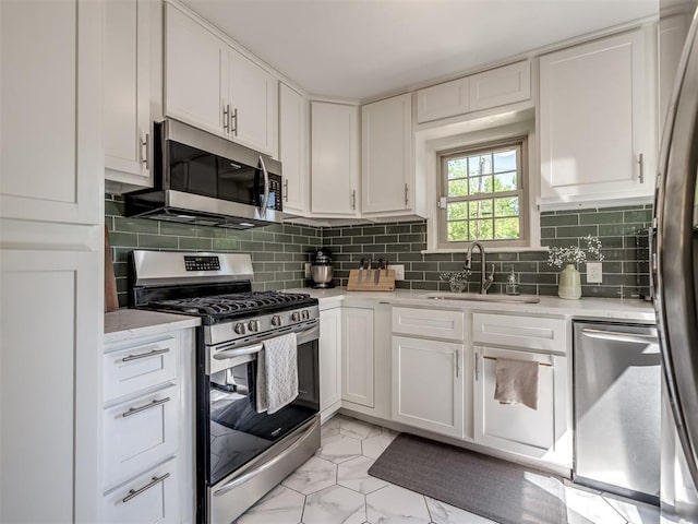 kitchen with backsplash, a sink, marble finish floor, stainless steel appliances, and white cabinetry