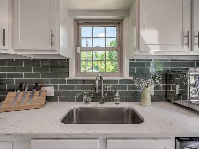 kitchen with white cabinetry, decorative backsplash, a sink, and dishwashing machine