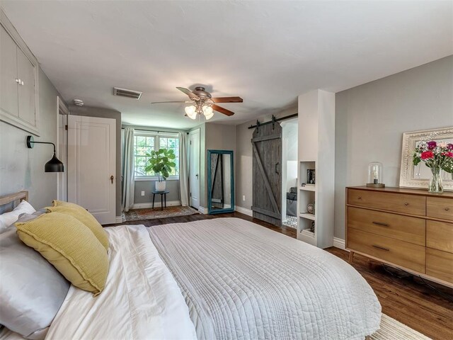 bedroom featuring ceiling fan, a barn door, baseboards, visible vents, and dark wood-style floors